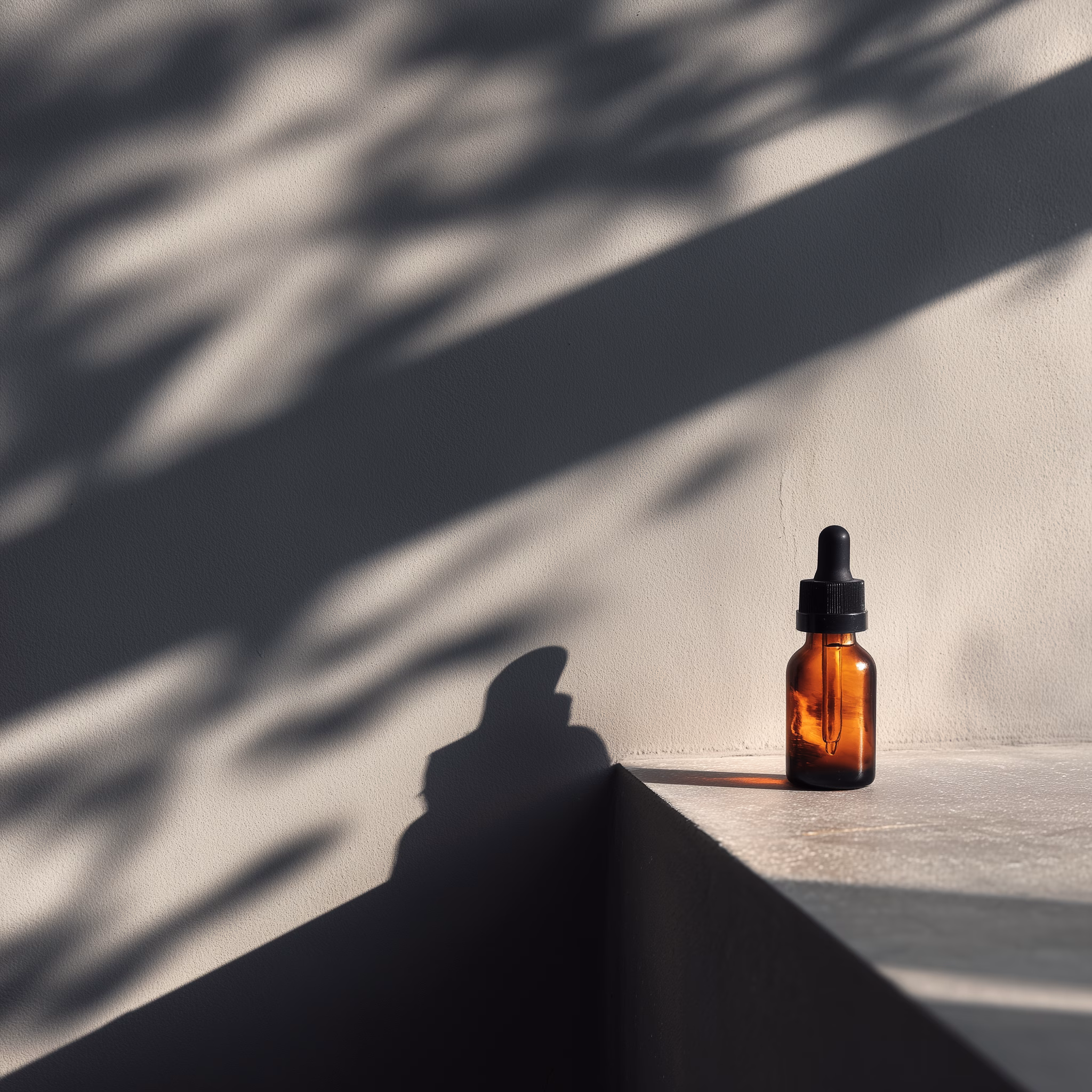 Amber glass dropper bottle casting a shadow on a minimalist surface with soft natural light and leafy shadows